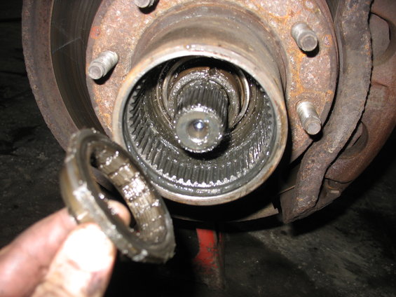 Close-up of a front wheel hub assembly with splines, a hand holds a greasy ring. Part of a brake rotor is visible