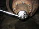1995 Ford C-350 (Centurion Conversions) - A socket wrench is being used to work on a vehicle's wheel hub assembly, with a warning label visible on a component.