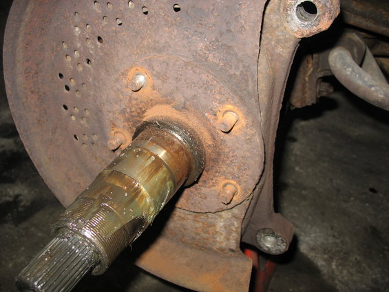 Rusted wheel hub with splined axle shaft covered in grease. Perforated brake rotor visible