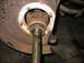 1995 Ford C-350 (Centurion Conversions) - This image shows a close-up view of a rusty front axle assembly, likely from a truck, with a driveshaft visible.