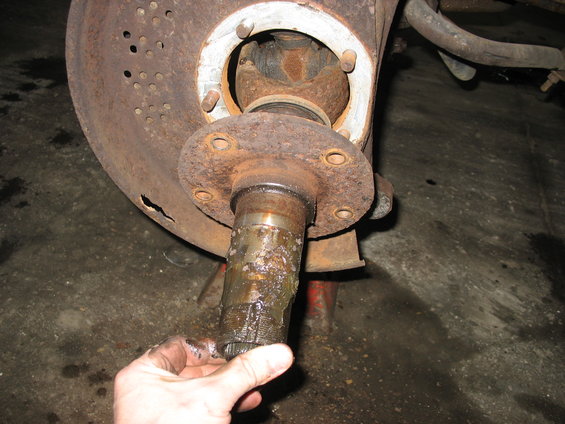 Front wheel hub assembly with spindle being held by a hand. Shows rust and grease