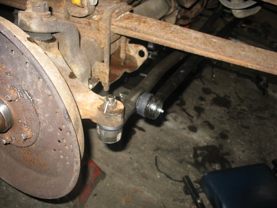 Close-up of a vehicle's front suspension and steering linkage, showing tie rod ends and a brake rotor