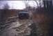 1978 Ford Bronco - A dark pickup truck navigates a challenging muddy road, its front grille and headlights visible.