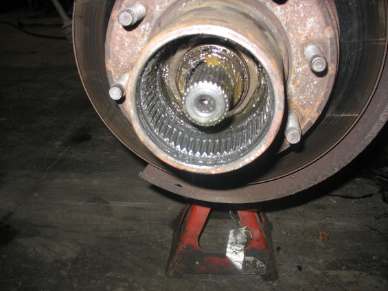 Close-up of a vehicle's front wheel hub assembly, showing gears and grease. The wheel is supported by a red jack stand