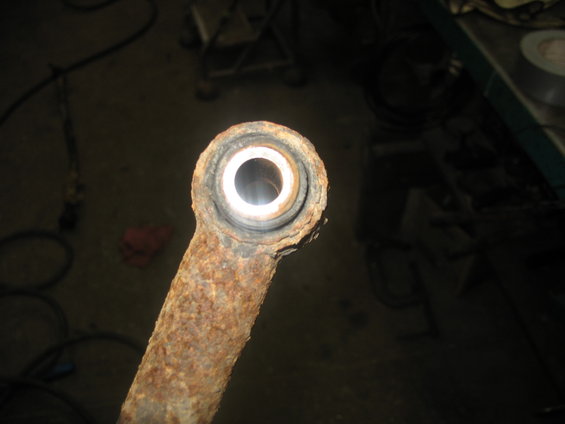 Rusted metal suspension arm with a worn rubber bushing visible
