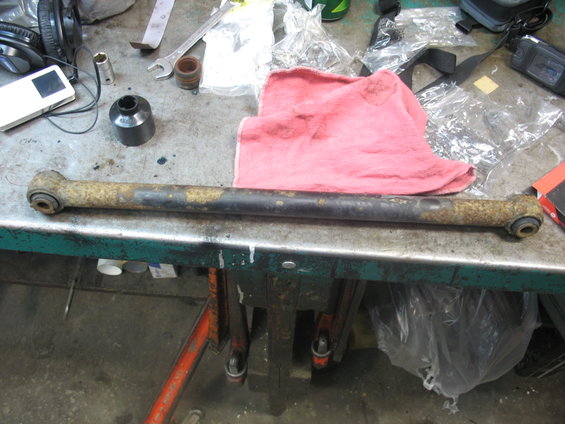 Rusted metal suspension arm with rubber bushings on a workbench
