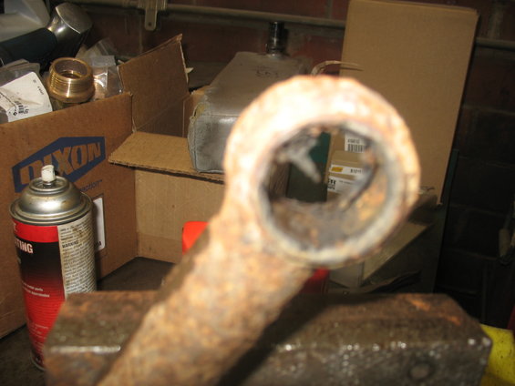 Close-up of a heavily rusted metal part held in a vise, with boxes and a spray can in the background