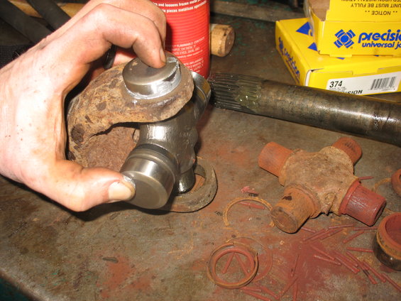 Hand holding a universal joint with a driveshaft and another U-joint on a workbench