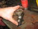 1995 Ford C-350 (Centurion Conversions) - Close-up of a hand holding a universal joint, with various driveshaft parts scattered on a rusty workbench.