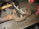 1995 Ford C-350 (Centurion Conversions) - Servicing a driveshaft universal joint with a grease gun and hammer on a workbench.