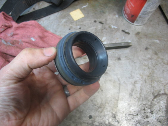 Hand holding a black and blue wheel bearing seal. A red can and a rag are in the background