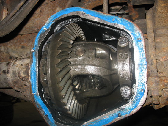 Close-up of an open differential housing with gears visible. Blue sealant is applied around the cover