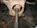 1995 Ford C-350 (Centurion Conversions) - Close-up of a heavily rusted front axle assembly, showing the bearing and splined shaft. Tools are scattered around the work area.
