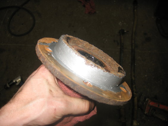 Hand holding a rusty wheel hub with a brake rotor attached. Some parts have been cleaned and painted silver