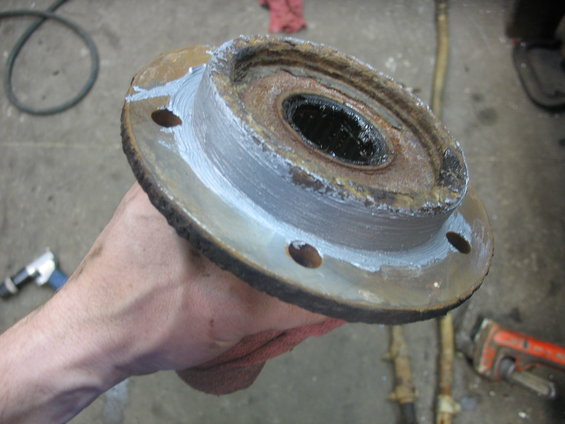 Rusted wheel hub with visible grease and repair paste, held in hand over a workshop floor