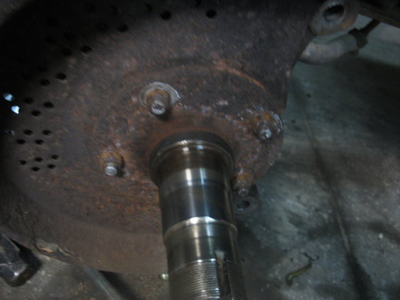 Close-up of a rusty metal component with several bolts and a shiny metal shaft extending from it