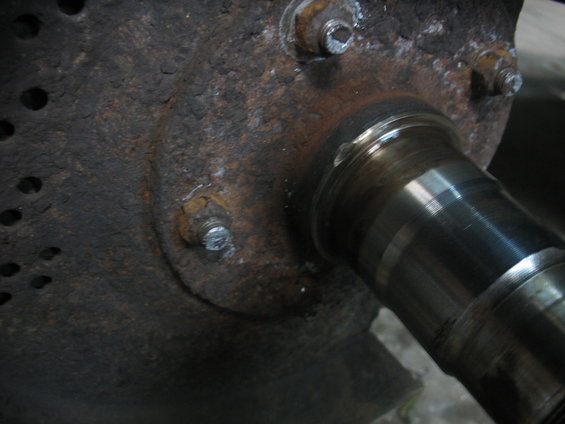 Close-up of a heavily rusted metal component with visible bolts and a shiny, grooved metal shaft extending to the right