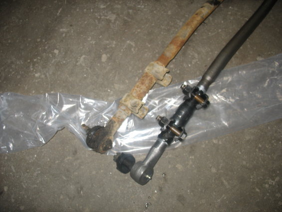 Old rusty steering linkage part next to a new one