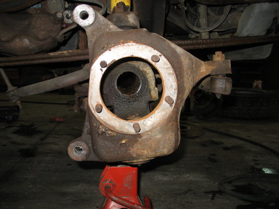 Rusted front wheel knuckle assembly on a red jack stand, part of a vehicle's suspension system