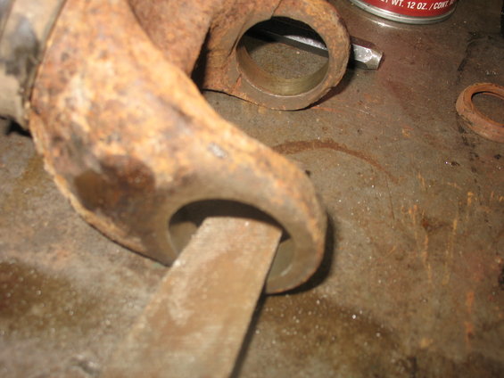 Heavily rusted metal component being worked on with a file. A can of lubricant is visible in the background
