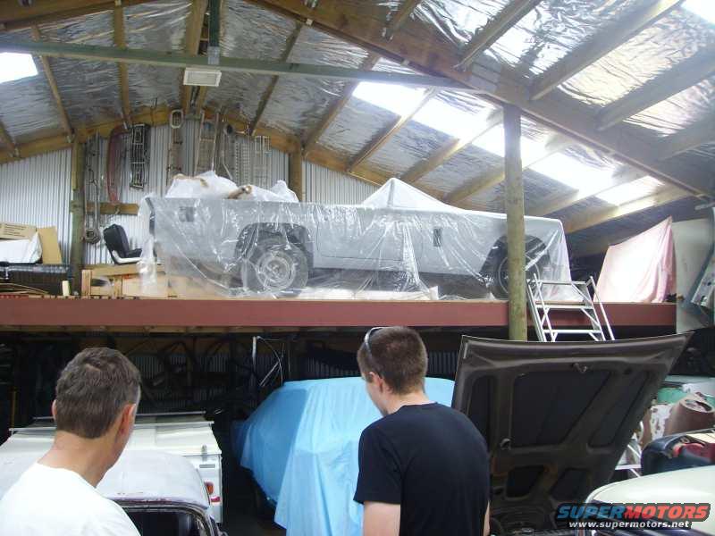 Car covered in plastic wrap on a raised platform inside a workshop