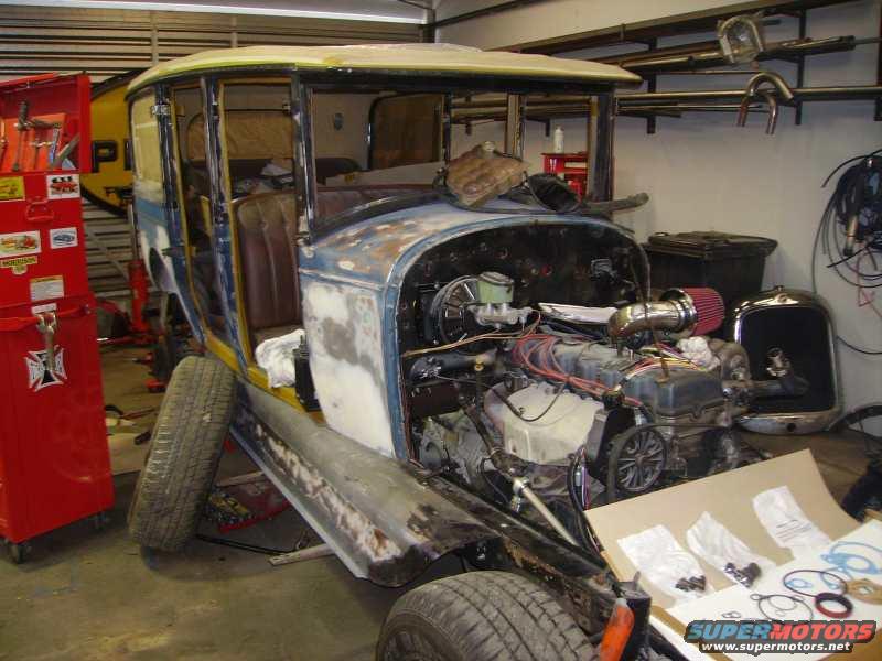 Vintage car body with engine exposed, undergoing restoration in a garage. Tools and parts are visible