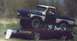 1978 Ford Bronco - A blue and white pickup truck is shown crushing a red sedan, which has white graffiti on its window.