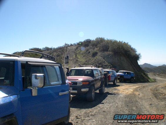 Line of blue and red Toyota FJ Cruisers on a dirt road with hills