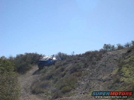 Blue 2007 Toyota FJ Cruiser climbing a steep dirt trail with brush on either side