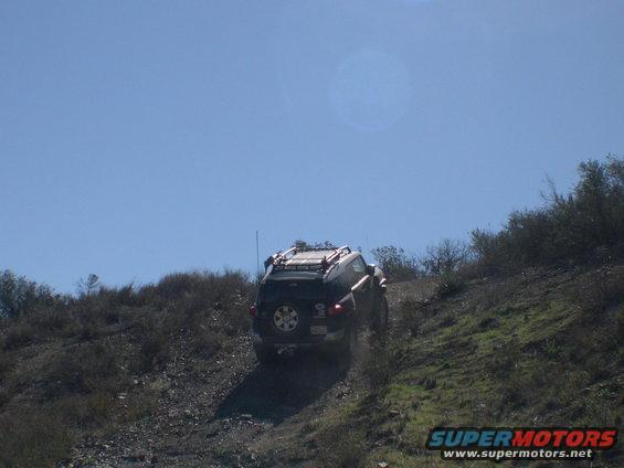 Black 2007 Toyota FJ Cruiser with roof rack driving up a dirt hill