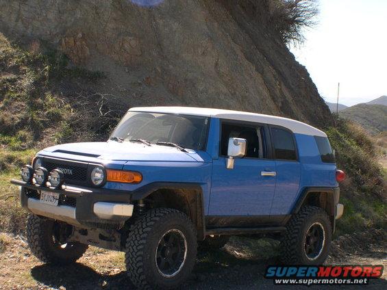 Blue 2007 Toyota FJ Cruiser parked on a dirt road with a rocky hillside behind it