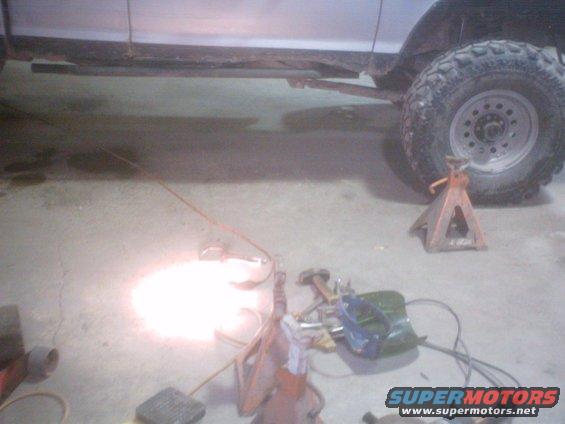 Silver truck side with large off-road tire on jack stands, welding equipment on floor