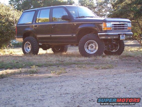 Lifted dark blue Ford Explorer SUV with aftermarket wheels and tires, parked on grass
