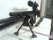 1985 Ford Bronco - A close-up view of a sniper rifle equipped with a scope and bipod, resting on a table.