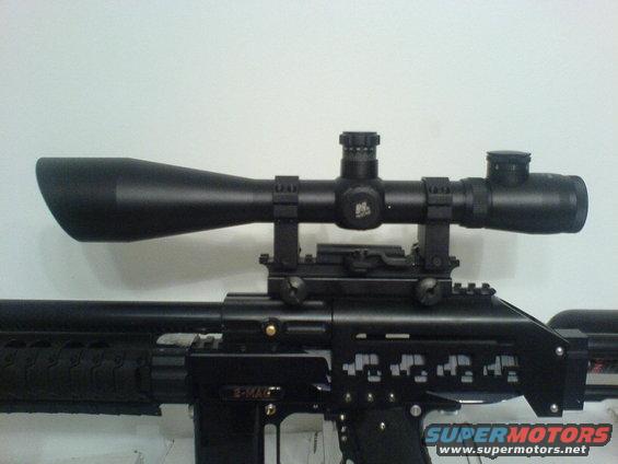 Black rifle with a large black scope mounted on top. The rifle has intricate cutouts on its side