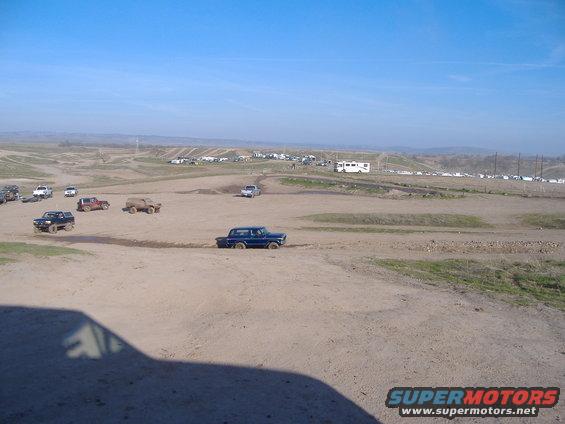 Several trucks and SUVs driving on a dirt track with spectators and RVs in the background
