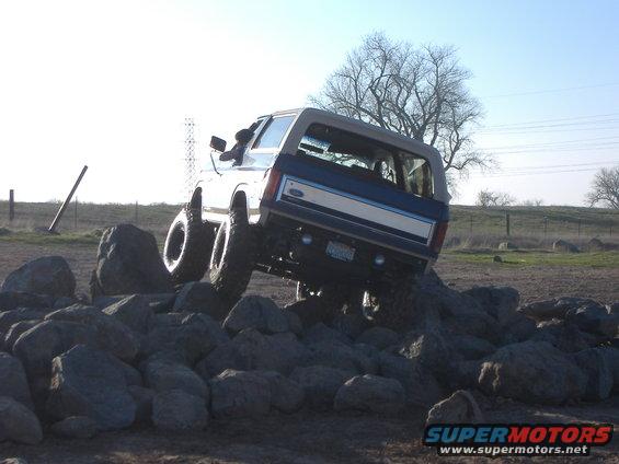 Ford Bronco climbing over rocks, driver visible inside
