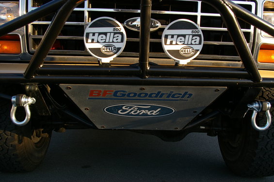Front view of a Ford Bronco with a roll cage, BFGoodrich skid plate, and Hella lights