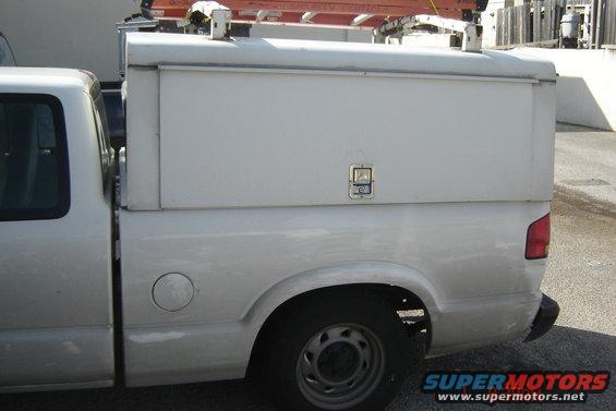 Side view of a white pickup truck with a white utility cap on the bed. Ladder rack on top of the cap