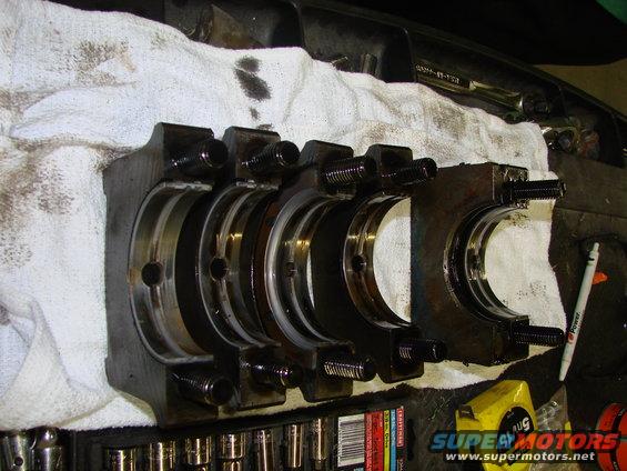 Engine crankshaft bearing caps with bolts and oil on a white cloth