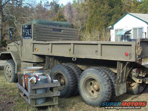 olive drab dump truck with "4 SALE" sign on window, parked in grassy area near house