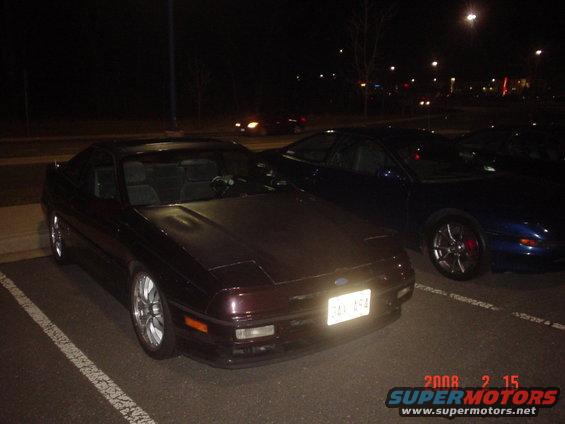 Dark colored Ford Probe parked at night, another blue car next to it