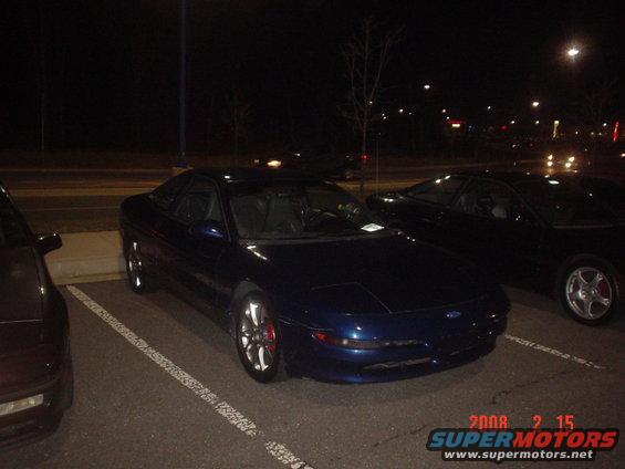 Dark blue coupe parked at night, front quarter view. Red brake calipers visible