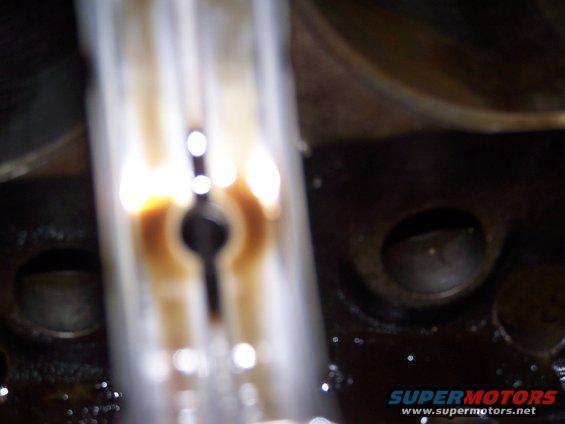 Close-up of an engine component with oil residue. The Supermotors.net logo is visible