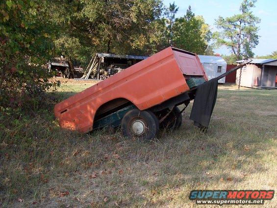 Orange truck bed on a trailer in a grassy yard with trees and sheds