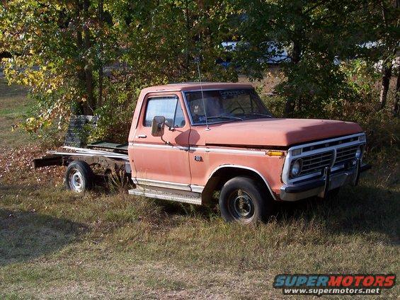 Old orange Ford truck cab and chassis parked in grassy area with trees