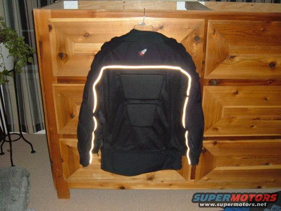 Black motorcycle jacket with reflective stripes hanging on a wooden dresser