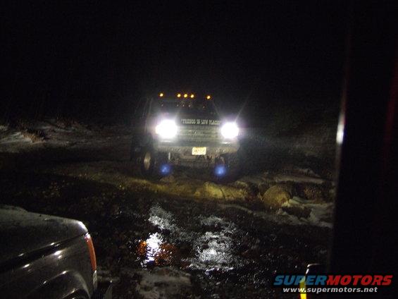 SUV driving at night with headlights on, another vehicle in foreground