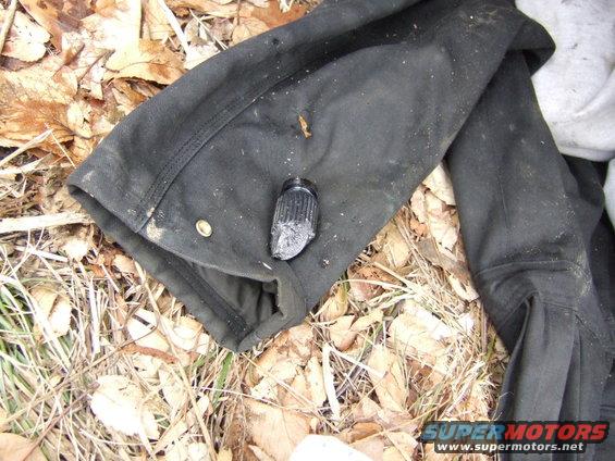 Black fabric with a broken black cap on the ground with leaves and grass