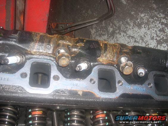 Engine cylinder head with spark plugs and exhaust ports, showing rust and grime